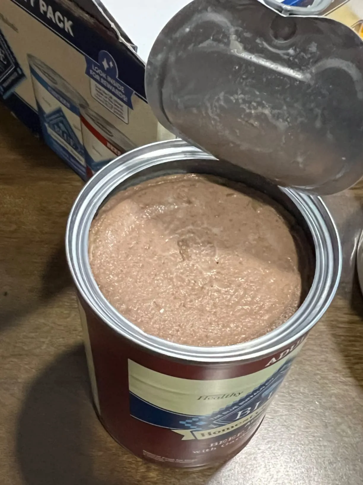 Rocket, healthy and alert, sitting next to a stack of empty Blue Buffalo cans ready for recycling